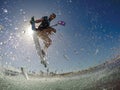 LOW ANGLE: Athletic young man splashes water at the camera while kitesurfing.