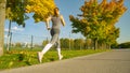 LOW ANGLE: Athletic young woman in gray sportswear jogs along colorful avenue.