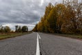 Low angle on autumn landscape. Old rural asphalt road in cracks with a wide white dividing strip on a background Royalty Free Stock Photo