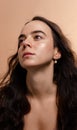 Beauty studio portrait of a beautiful young woman with long dark hair and natural glowing skin on a beige background.