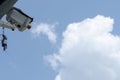 Low-angle, close-up view of a CCTV on a pole against a fluffy cloud and blue sky Royalty Free Stock Photo