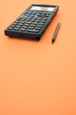 Low angle closeup of a graphing calculator and a tiny pen isolated on an orange background