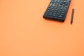 Low angle closeup of a graphing calculator and a tiny pen isolated on an orange background