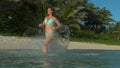 LOW ANGLE: Glassy droplets fly in air as woman runs in the shallow part of sea Royalty Free Stock Photo