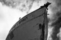Low angle grayscale shot of an abandoned boat under sky with clouds