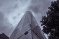 Low angle greyscale shot of a high skyscraper with mirror windows under the storm clouds