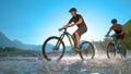 LOW ANGLE: Guys riding ebikes along the shallow river and splashing water