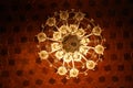 Low angle of the luxurious, hanging chandelier illuminating a red, Indian mosque ceiling