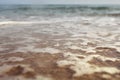 Low angle photo from ground level - beach with shallow water and white foam over sand, wet drops in air, blurred ocean in distance Royalty Free Stock Photo