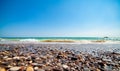 Low angle photo of pebble stones on the seashore, waves and the blur sky