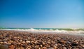 Low angle photo of pebble stones on the seashore, waves and the blur sky