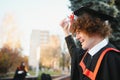 Low angle portrait of happy triumphant male graduate standing near university holding up diploma. From below of young