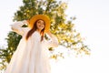 Low-angle portrait of smiling young woman in straw hat and white dress standing posing on beautiful meadow of green Royalty Free Stock Photo