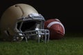 Low angle selective focus of football and gold helmet on grass with dark background