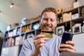 Low angle shop of handsome young adult smiling man holding credit card and using phone doing online payment, purchasing and Royalty Free Stock Photo