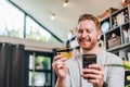 Low angle shop of handsome young adult smiling man holding credit card and using phone doing online payment, purchasing and Royalty Free Stock Photo