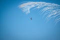 Low-angle shot of an aircraft performing an air show against a clear blue sky with smoke