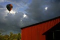 Low angle shot of a colorful hot air balloon in the sky over a wooden barn Royalty Free Stock Photo