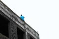 Low angle shot of a male in a blue shirt sitting on the roof of an abandoned building