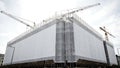 Large white building under construction with multiple cranes against a cloudy sky Royalty Free Stock Photo