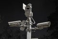 Low-angle shot of multiple old security cameras on a metal pole against a dark sky. Royalty Free Stock Photo