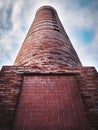 Low angle shot of a red brick industrial smoke stack against a cloudy sky Royalty Free Stock Photo