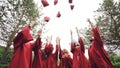 Low angle shot slow motion of happy grads throwing traditional hats in the sky, laughing and having fun on graduation