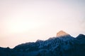 Low angle shot of the sun shining on a peak of a snow covered rocky mountain Royalty Free Stock Photo