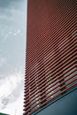 Low angle shot of a tall modern building in a red facade under a cloudy sky Royalty Free Stock Photo