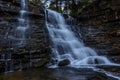 Low-angle shot of a waterfall, flowing into smooth stone texture and coming into a pond