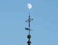 Low angle shot of  a  weather vane or wind wane on blue sky background with a moon Royalty Free Stock Photo