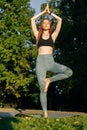Low-angle shot of young woman with closed eyes doing yoga in tree pose, raising hands overhead. Royalty Free Stock Photo
