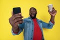 Waist up of funny African man keeping cupholder and smartphone in arms