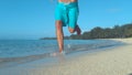 LOW ANGLE: Unknown man in blue boardshorts running on the exotic sandy beach.