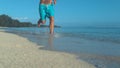 LOW ANGLE: Unrecognizable man runs barefoot down beautiful white sand beach.