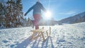 LOW ANGLE: Unrecognizable young woman runs along a snowy meadow pulling her sled