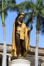 Low-angle vertical of King Kamehameha statue in downtown Honolulu, palm trees, clear sky background