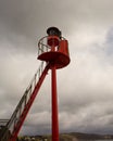 Low-angle vertical shot of a red warning beacon with ladder at harbor entrance Royalty Free Stock Photo