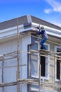 Asian builder worker on wooden scaffolding is painting roof structure of modern house against blue sky