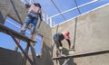 Low angle view of 2 Asian builder workers on wooden scaffolding are plastering concrete wall in house construction site Royalty Free Stock Photo