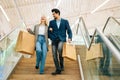 Low-angle view of cheerful beautiful young couple holding shopping paper bags with purchases and walking down stairs Royalty Free Stock Photo