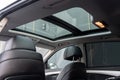 Low angle view of clean panoramic glass roof of deluxe automobile. Light interior panelling and black leather seats