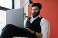 Low-angle view of confident Indian business man in formalwear working typing on laptop sitting on chair in light Royalty Free Stock Photo