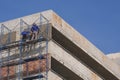 2 construction workers on high scaffolding are plastering cement wall on rooftop of parking garage building in construction site Royalty Free Stock Photo