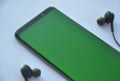 Low angle view of curved screen mobile phone with green screen and black color earphone over white background Royalty Free Stock Photo