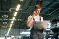 Low-angle view of focused handsome young mechanic male wearing uniform reading clipboard and talking on mobile phone.