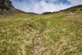 Low angle view of grass covered slope with path towards mountain Royalty Free Stock Photo