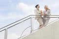 Low angle view of happy businesswomen discussing while standing by railing against sky Royalty Free Stock Photo
