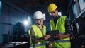 Low angle view of industrial inspectors with tablet doing a general check up and talking indoors at metal workshop.