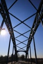 Low angle view on isolated symmetrical industrial steel bridge deck against blue sky with cross struts and metal beams, sun burst